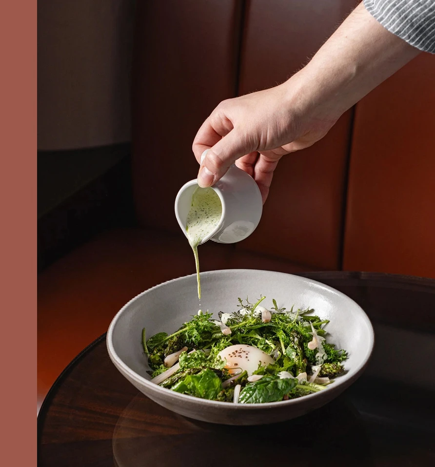 Hand pouring dressing onto a salad in a grey bowl